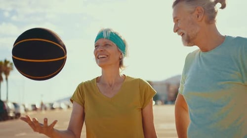 Smiling Senior Couple Tossing Basketball on Beach Parking Lot