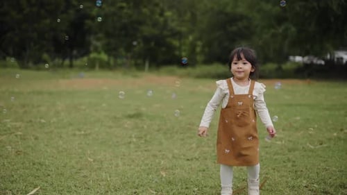 slow motion of happy toddler girl running and playing soap bubble in grass field