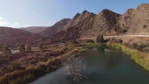 A drone chasing birds flying over a river winding past a mountain.