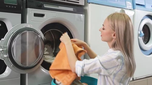 Woman Loads Laundry into Washing Machine at Laundromat