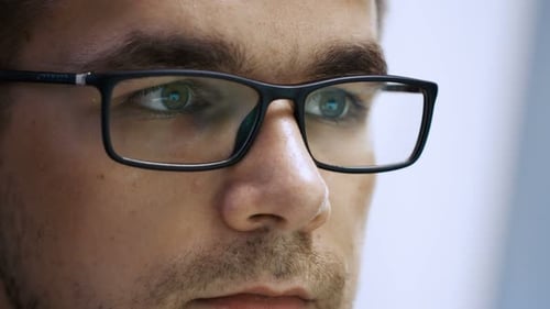 Close-up of a Young Male Wearing Glasses and Computer Screen Reflect in Them.