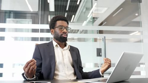 African American businessman in a formal suit practicing meditation with closed eyes in office