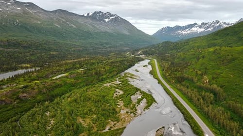 Cars go by the highway along the shallow river flowing in the valley.