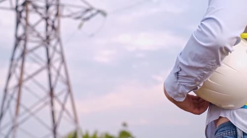 A designer inspects a high voltage tower. An engineer in a hard hat servicing a power transmission p