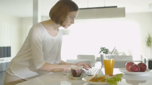 Young woman is using a laptop computer in the morning at home kitchen area.