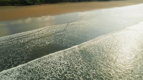 Top view of foaming ocean waves rolling over dark sand on a tropical shore
