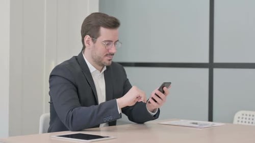 Businessman Browsing Internet on Smartphone in Office