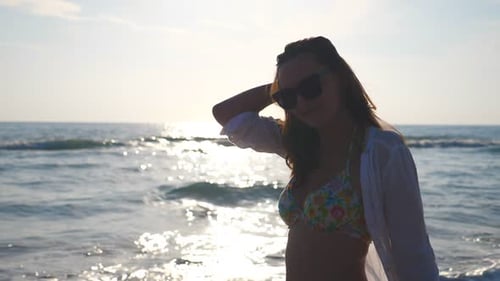 Portrait of Beautiful Girl in Bikini and Shirt Walking Along Seashore and Playing with Her Hair