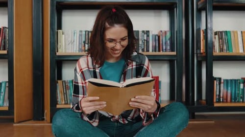 Young Woman Student Reading a Book in the Library Sitting on the Floor Students in a Good Mood