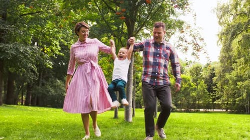 Family Swinging Child While Walking in Green Park