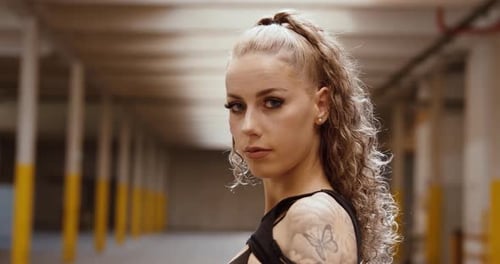 Tattooed woman in industrial hall looking over shoulder – camera moves in slowly