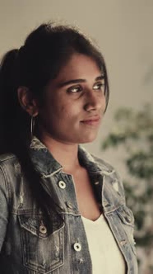 Une femme indienne attentionnée avec une queue de cheval regarde une fenêtre lumineuse