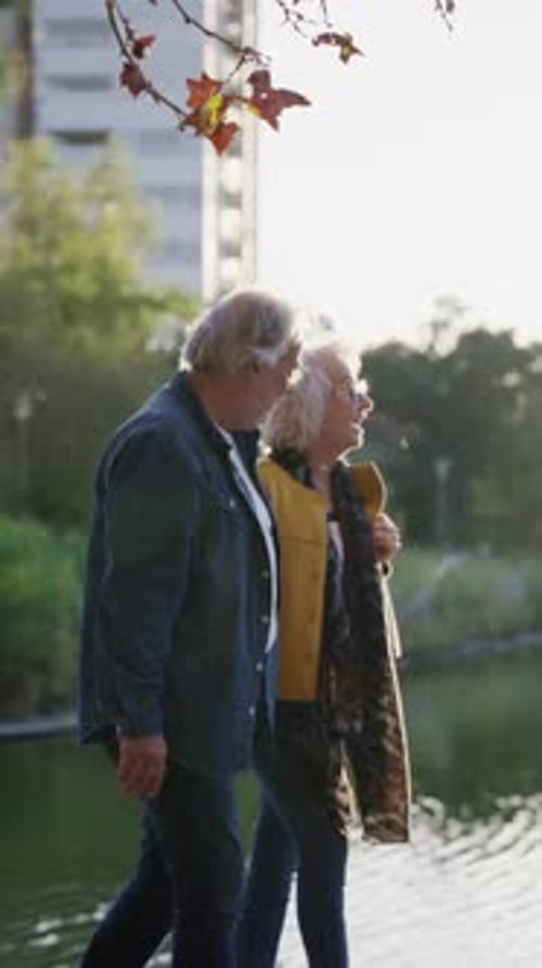 Feliz pareja mayor caminando por el lago en un parque urbano