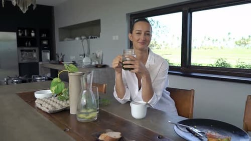 Woman Drinks Green Juice at Kitchen Table