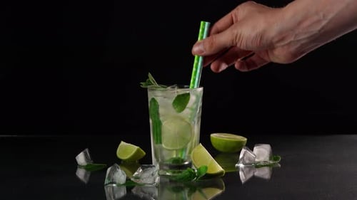 A close-up of the bartender's Hand Putting cocktail Tubes in a glass of Mojito
