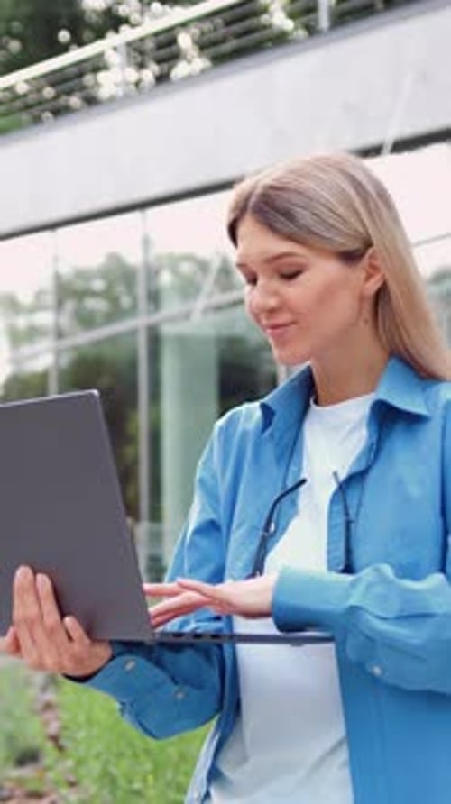 Professional Confident Businesswoman Typing on a Laptop Outdoors Near a Modern Glass Office Building