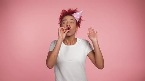 Cheerful Woman Blowing Party Horn on Pink Background