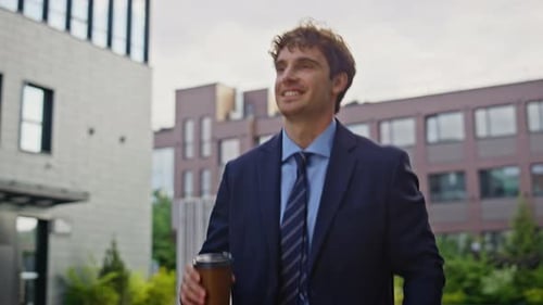Smiling Young Adult in Suit Walking with Coffee