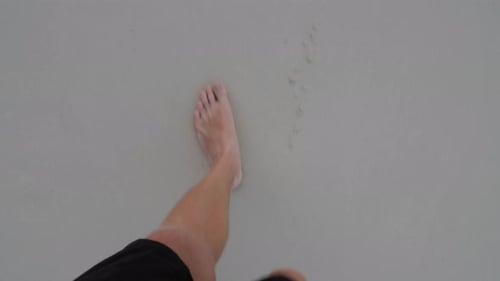 Male feet walking barefoot on sand filmed looking down from the man's point of view