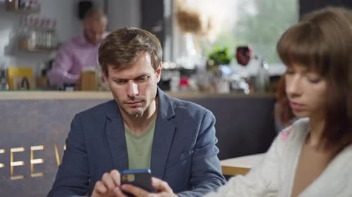 A Man on a Date with a Girl in a Cafe Scrolls and Texts on the Phone