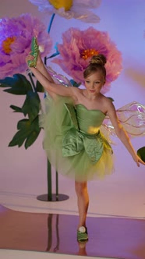 Child in Green Fairy Dress with Translucent Wings Posing Among Giant Flowers