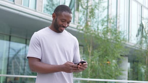 African American Man Holding Smartphone Touch Screen Typing Scroll Page on Urban Street in City Guy