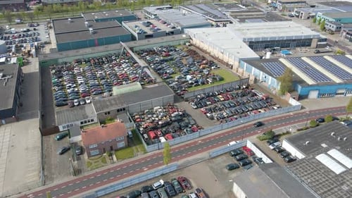 Luftbild eines Autos, das an einem Schrottplatz voller Autowracks auf industriellem Gelände vorbeifährt