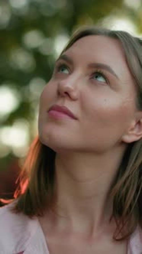 Gros plan d'une femme souriante et levant les yeux pensivement dans un cadre naturel