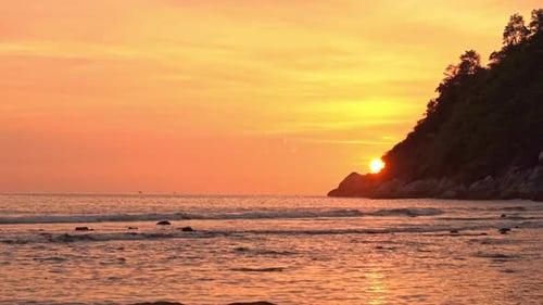 Amazing romantic view of sun hiding behind sea cliff at sunset.