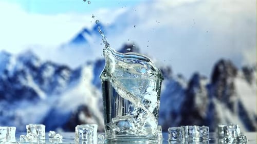 An Ice Cube Falls Into a Glass of Water with Splashes