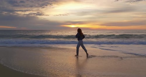 Silhouette of a Woman Running Along the Ocean Coast Barefoot on a Breaking Wave at Sunset The
