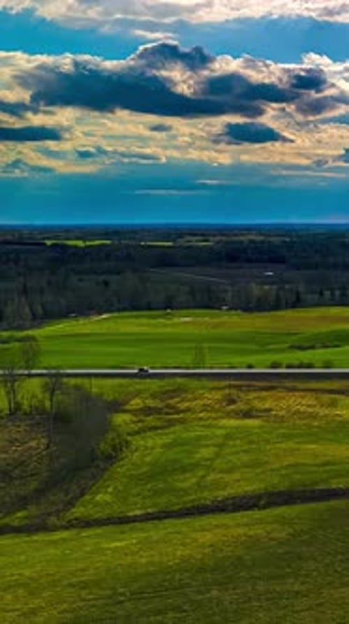 Vertical aerial time lapse of traffic on country road and moving clouds in rural Latvia