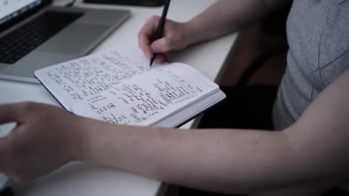 Handwriting in Notebook with Pen and Laptop in Background