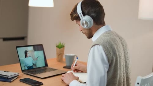 Young Man Attends Online Class and Writes Notes