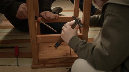 Garçon aidant son père à assembler une chaise en bois, avec tournevis