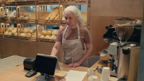 Senior Female Worker Using Cash Register in Bakery