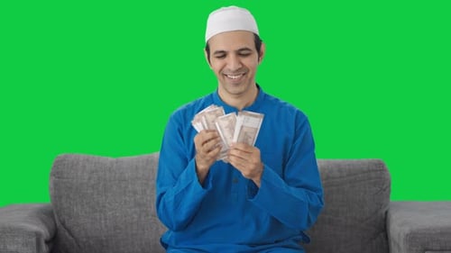 Happy Muslim man counting money Green screen