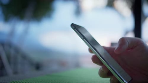 Hände eines Mannes, der sein Handy benutzt und draußen im Hintergrund seiner Apps surft