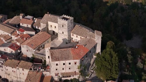 Stunning aerial view of a historic village with a medieval tower nestled in lush greenery at sunset