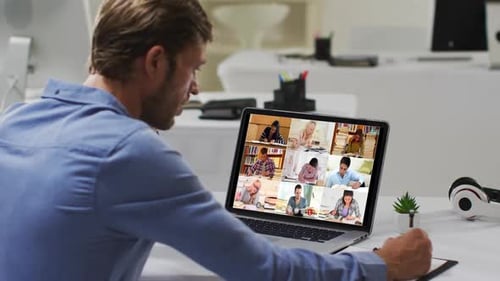 Man on Video Call Taking Notes at Desk