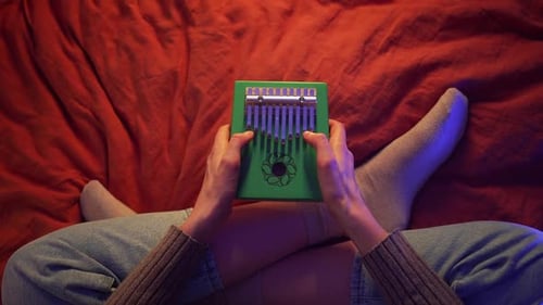 Female Musician Sitting Crosslegged on Red Blanket Playing Green Kalimba with Gentle Finger