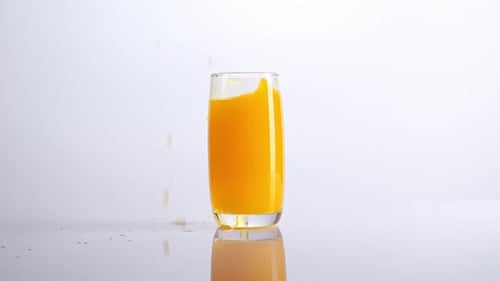 Ice Cube Falling In A Glass Of Orange Juice On The Light White Screen Background In The Studio