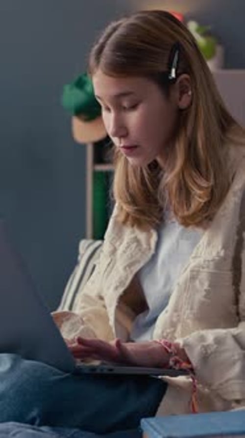 Teen girl uses laptop sitting on bed