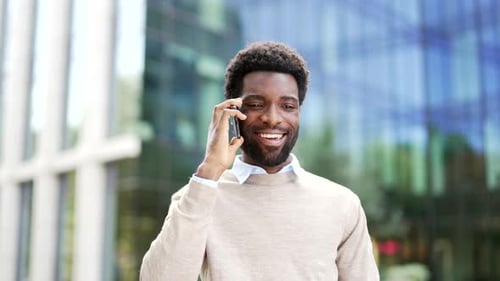 Confident african american businessman talking on mobile phone standing on city street near office