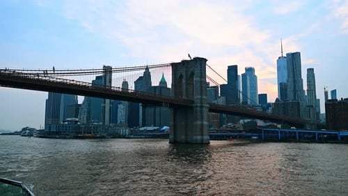 Approaching the Brooklyn Bridge by the boat. Low angle view at the famous landmark at dusk time.