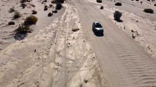 A wide panning up drone shot of a car driving down a dirt road in a desert landscape in Southern Cal