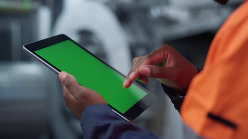 Nahaufnahmetechniker hält Greenscreen-Tablet-Computer in der modernen Fabrik in der Hand. Unbekannter afrikanischer Ame...
