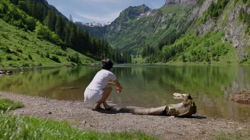 Woman sits by Talalpsee lake in Filzbach, surrounded by mountains and lush greenery, meditating