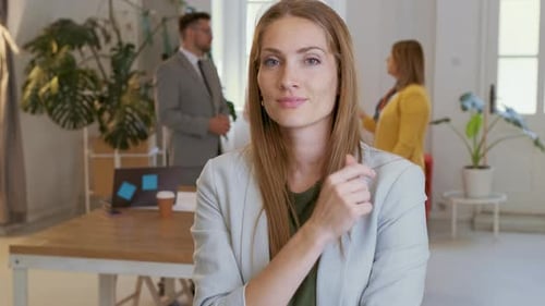 Portrait of smiling businesswoman in office with her colleagues in background.