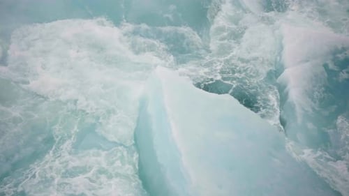 Topdown View of Turquoise Seawater Churning Around Fractured Ice Slabs and Drifting Floes Revealing